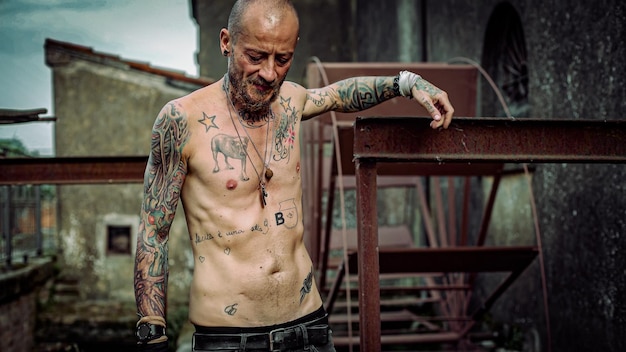 Frustrated man with tattooed body in an abandoned site old\
machinery