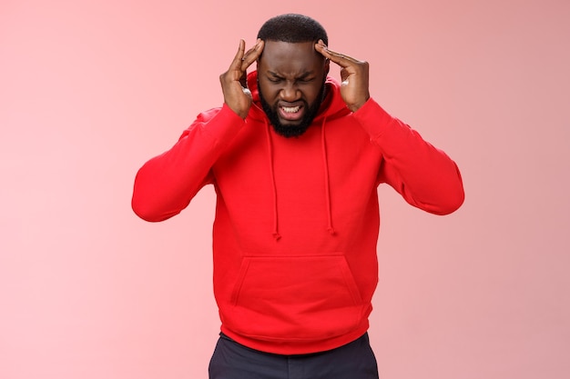 Frustrated pressured stressed-out young african-american businessman frowning cringing painful feeling holding hands head temples suffer miragine bothering headache, standing pink background.