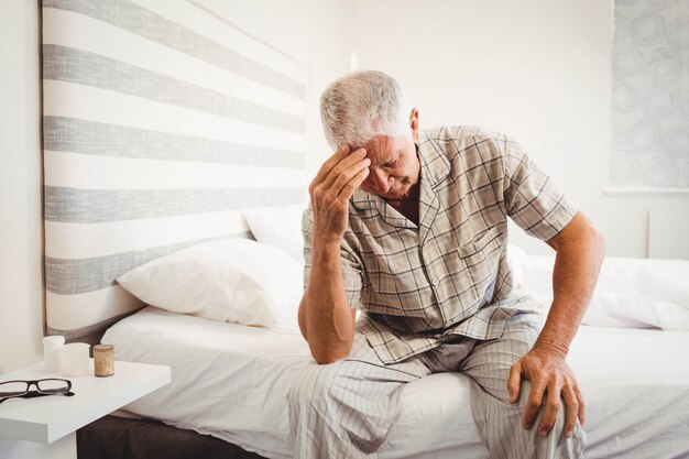 Frustrated senior man sitting on bed in bedroom