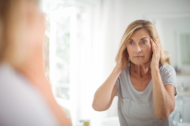 Frustrated senior woman looking at mirror