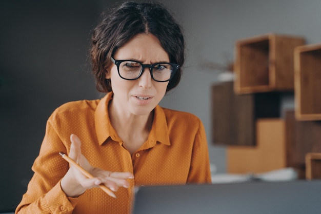 Frustrated spanish female freelancer looking angry on laptop screen while working from home