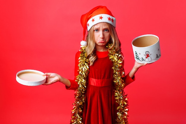 Frustrated teenage girl in santa hat and tinsel on neck opening box,