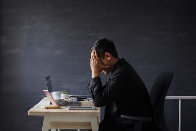 Frustrated and unhappy businessman in suit sitting on office desk with hand on head