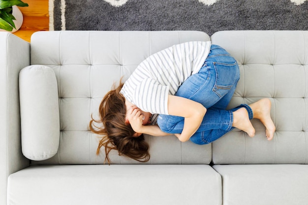 Frustrated woman covering face and crying lying on sofa at home alone