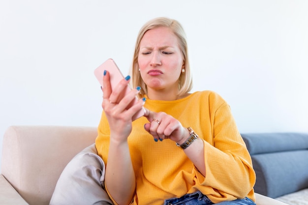 スマートフォンが機能しない問題を抱えている女性自宅のオフィスデスクに座っている怒った混乱した女性電池が消えたり壊れたりしてイライラした女性携帯電話のメッセージで悪いニュースを受け取った