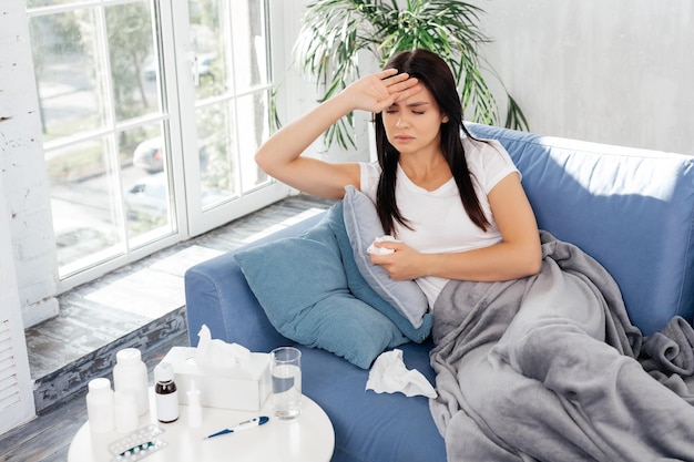 Frustrated woman lying under blanket while keeping her hand on forehead and looking down