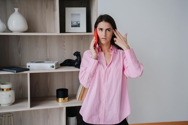 Photo frustrated young brunette talking by phone with upset expression dressed in pink shirt annoyed