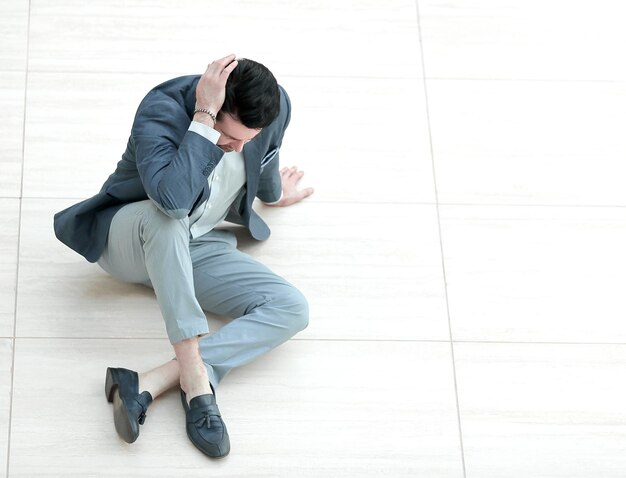 Frustrated young businessman sitting on the floor and looking down