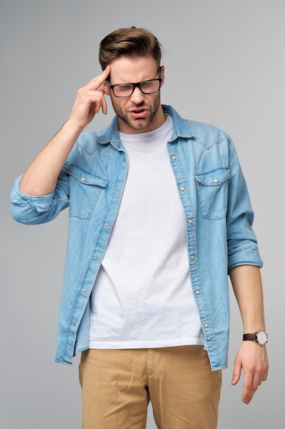 Frustrated young caucasian man in jeans shirt touching head with hand while standing