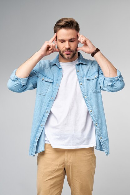 Frustrated young caucasian man in jeans shirt touching head with hand while standing  