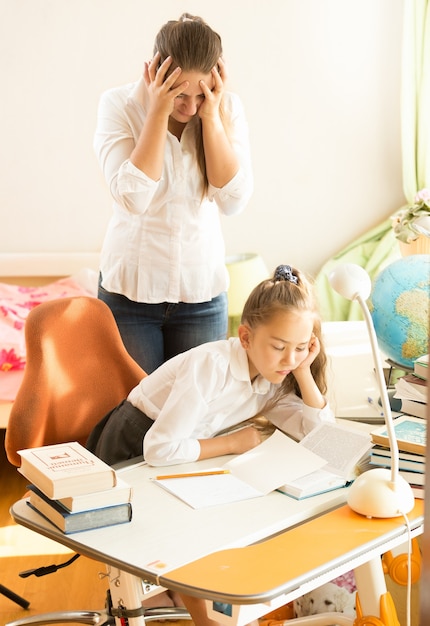 Frustrated young mother looking daughter sleeping while doing homework