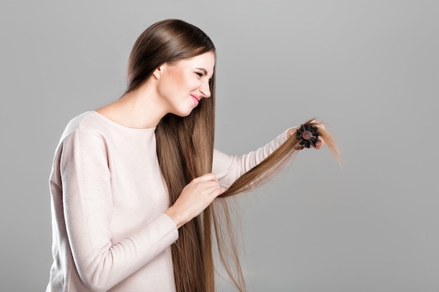 Frustrated young woman combing tangled long natural hair with hairbrush