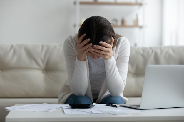 Frustrated young woman holding head in hands feeling stressed about financial problems Unhappy millennial girl having troubles with managing budget termination banking letter bankruptcy concept