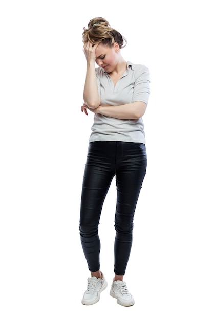 A frustrated young woman is standing Beautiful blonde in black leggings a gray tshirt and white sneakers Stress depression and negativity Full height Isolated on white background Vertical