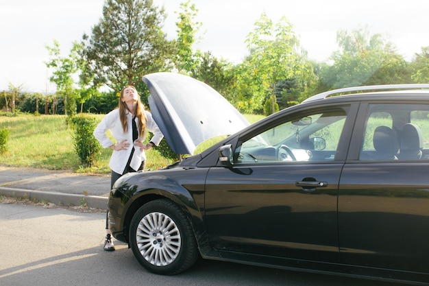 Frustrated young woman looking at broken down car engine on street