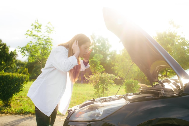 Photo frustrated young woman looking at broken down car engine on street