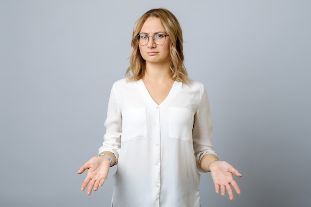 Frustrated young woman shrugs shoulders with her arms out isolated