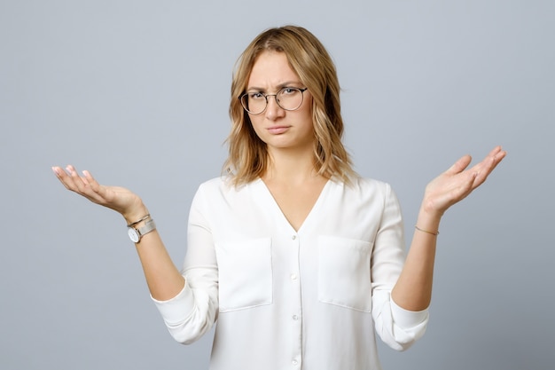 Frustrated young woman shrugs shoulders with her arms out isolated