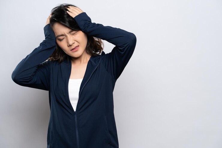 Photo 灰色の背景に立って頭を握るフード付きのシャツを着たイライラした若い女性