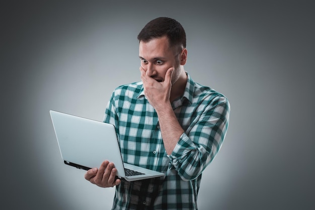 Foto frustreerde zakenman met een laptop bedekt zijn gezicht met zijn hand op een grijze achtergrond.