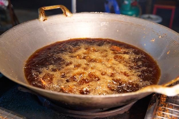 Fry in a large wok with dark oil at a street food market in Thailand