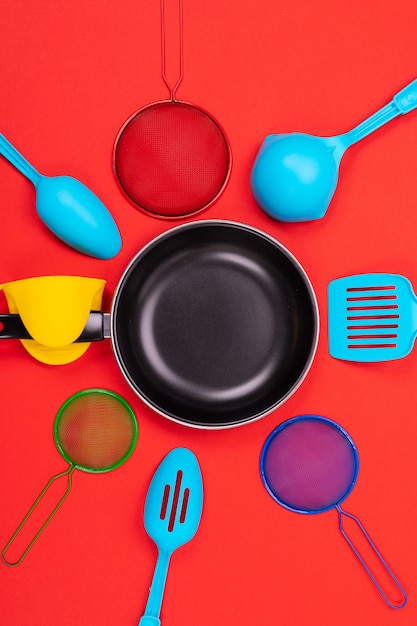 Frying pan in the center with cooking utensils around on red