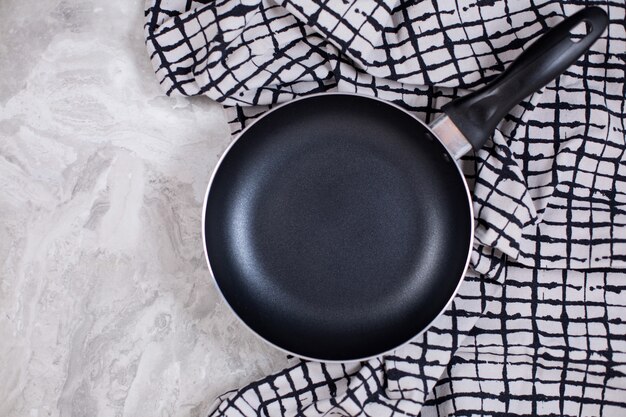Frying pan or skillet with kitchen towel on White marble. Top view.