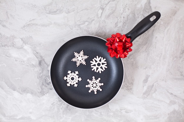 Frying pan or skillet with snowflakes on marble table. Top view. Copy space.