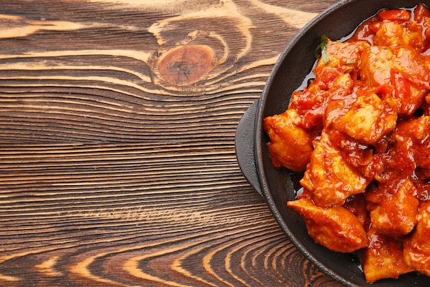 Frying pan with delicious chicken tikka masala on wooden table