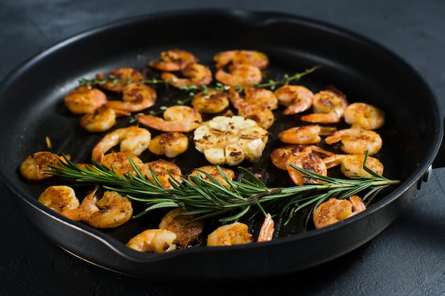 Frying pan with fried king prawns and sprigs of rosemary and thyme.