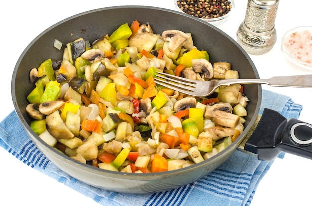 Frying pan with fried seasonal vegetables and mushrooms on white. 