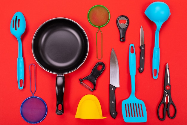 Frying pan with kitchen utensils on red