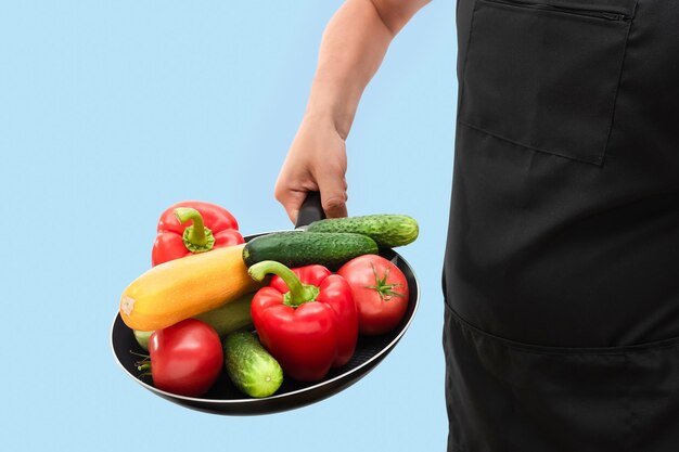 Frying pan with organic vegetables in the hands of a cook isolated on a blue background