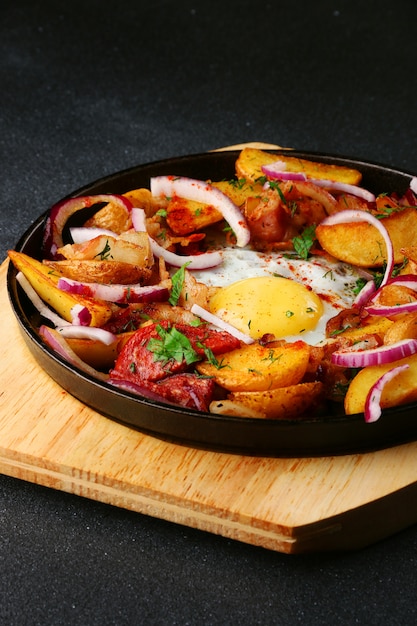 Frying pan with potatoes meat and egg on black concrete background. mexican food