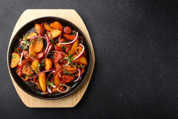 Frying pan with potatoes meat and onion on black concrete background  