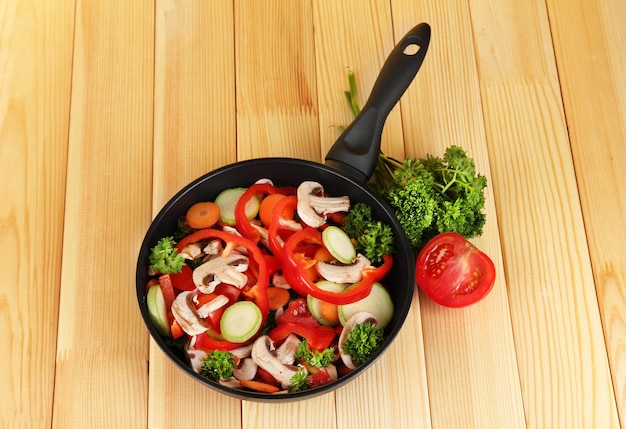 Frying pan with vegetables on wooden background