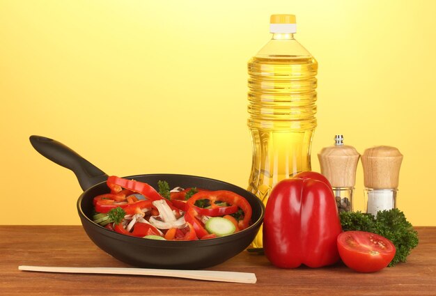 Frying pan with vegetables on yellow background