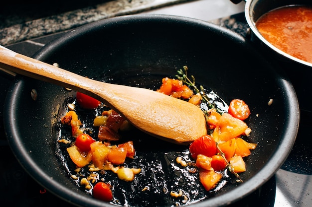 Frying tomatoes and herbs on a pan top view wooden spoon