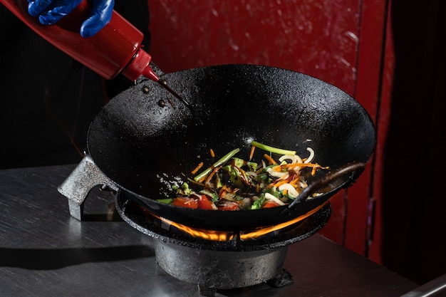 Frying vegetables in a wok pan onions, broccoli, tomatoes cherry, carrot, asparagus.