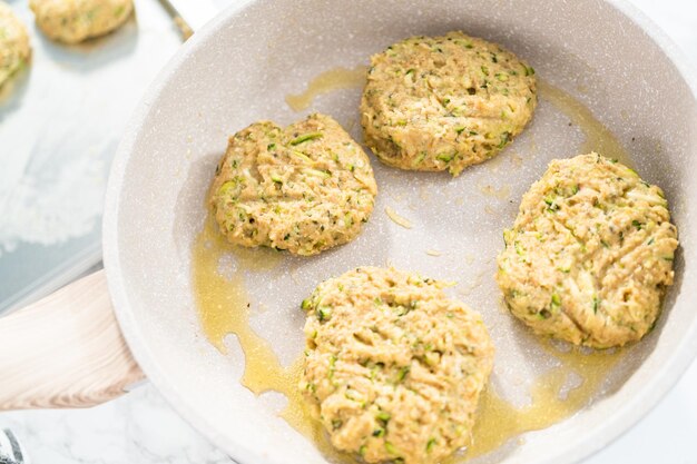 Frying zucchini cakes in olive oil on a frying pan.