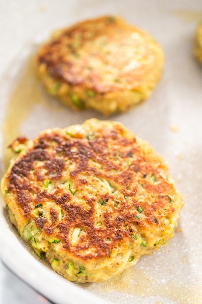 Frying zucchini cakes in olive oil on a frying pan.