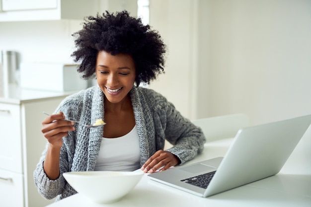 즐거운 하루를 위한 에너지 충전 집에 있는 부엌에서 아침 식사를 즐기면서 인터넷을 서핑하는 젊은 여성의 샷