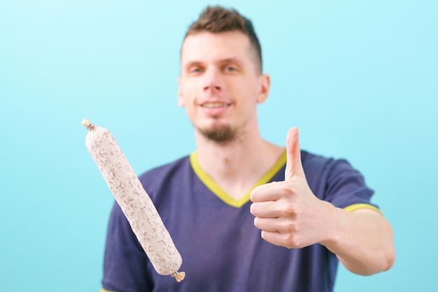 Fuet dried sausage in front of smiling man who shows thumb up on a blue