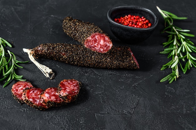 Fuet, Salami and a sprig of rosemary. Traditional Spanish sausage. Black background. Top view. Space for text