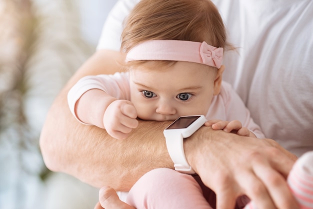 Full of attention. Sweet cute involved baby girl lying in hands of the father and looking away while expressing interest and joy