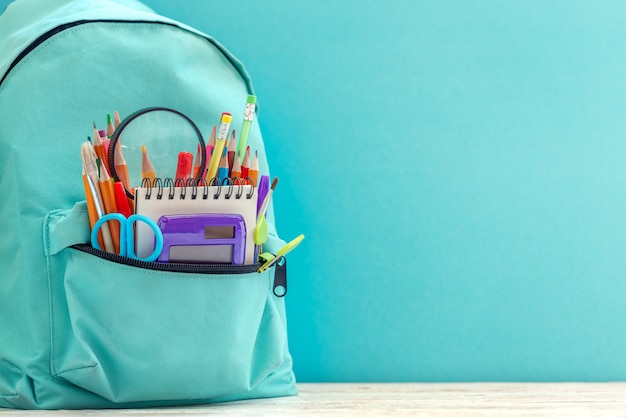 Full blue School Backpack with different supplies on blue background.