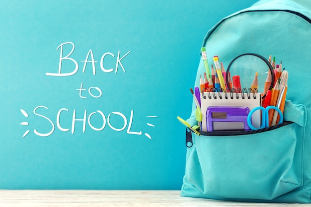 Full blue School Backpack with different supplies on blue background.