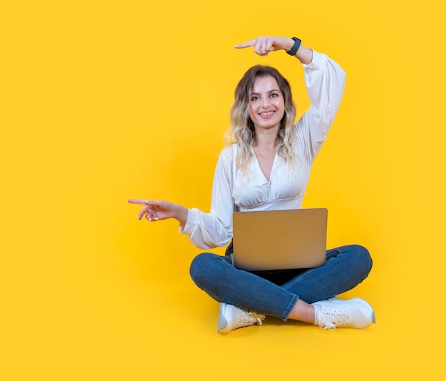 Full body blonde young beautiful woman sit floor with laptop pc computer pointing aside copy space