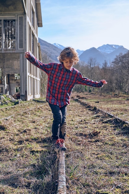 Full body of boy in casual wear balancing on rail going through rural grassy abandoned valley surrounded by mountains