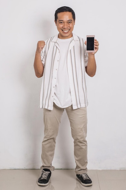 Full body of casual asian man in shirt showing his smartphone blank screen with winning gesture